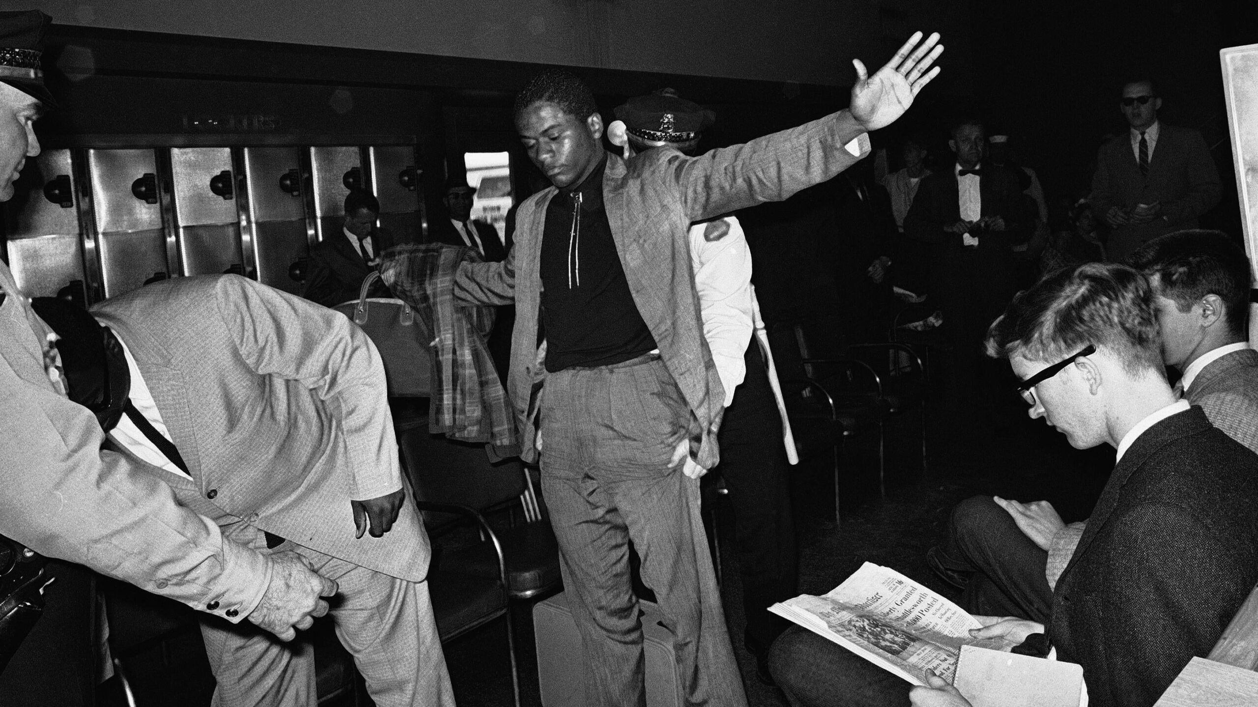 A policeman searches a Freedom Rider in the white waiting room of the bus station, May 28, 1961, Jackson, Miss. Eight more Riders were arrested when they failed to heed orders to move on. Seated at right are two more of the group, including one white man. - Associated Press