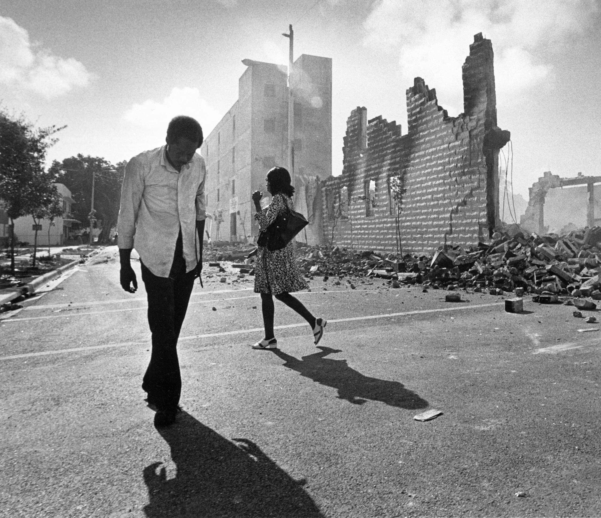 In this May 19, 1980, photo, people walk past ruins in the Culmer section of Miami after rioting over the acquittal of four police officers charged with the 1979 beating death of Arthur McDuffie, a black motorcyclist. When future Virginia Gov. Ralph Northam and future Attorney General Mark Herring admitted dressing up in blackface in the 1980s racial stereotypes and racist imagery in popular culture seemed to be everywhere. There also was racial unrest and historic elections of black mayors. (AP Photo/Kathy Willens, File) - Associated Press